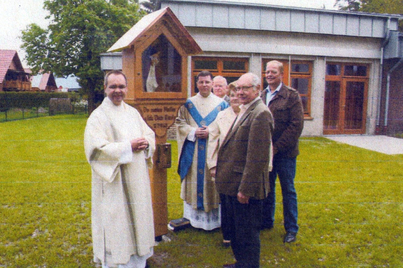 Zwei Geistliche und mehrere Gäste vor dem Bildstock und dem Kindergartengebäude